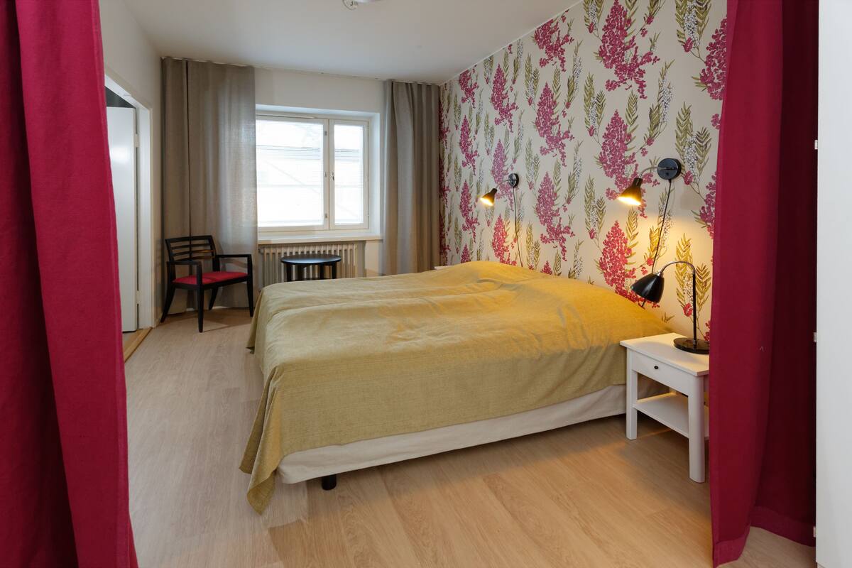 A bedroom with a bed, a chair, a nightstand, and a window.