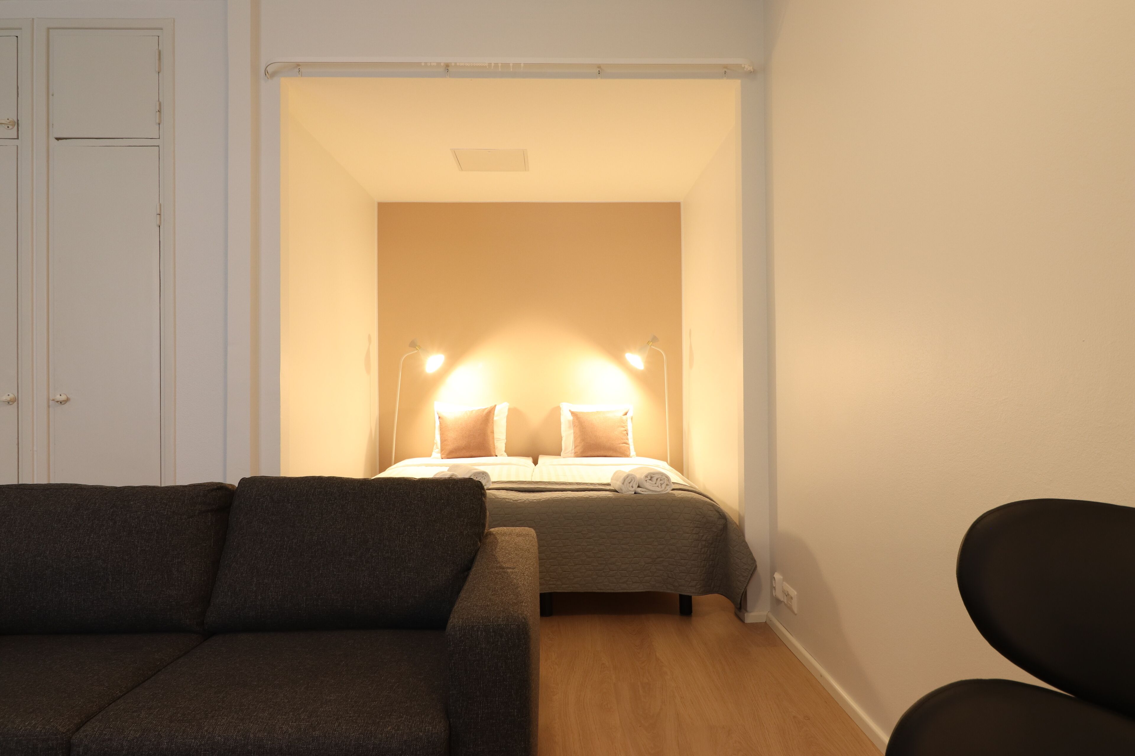 Un dormitorio con cama, lámparas de noche, sofá y sillón.