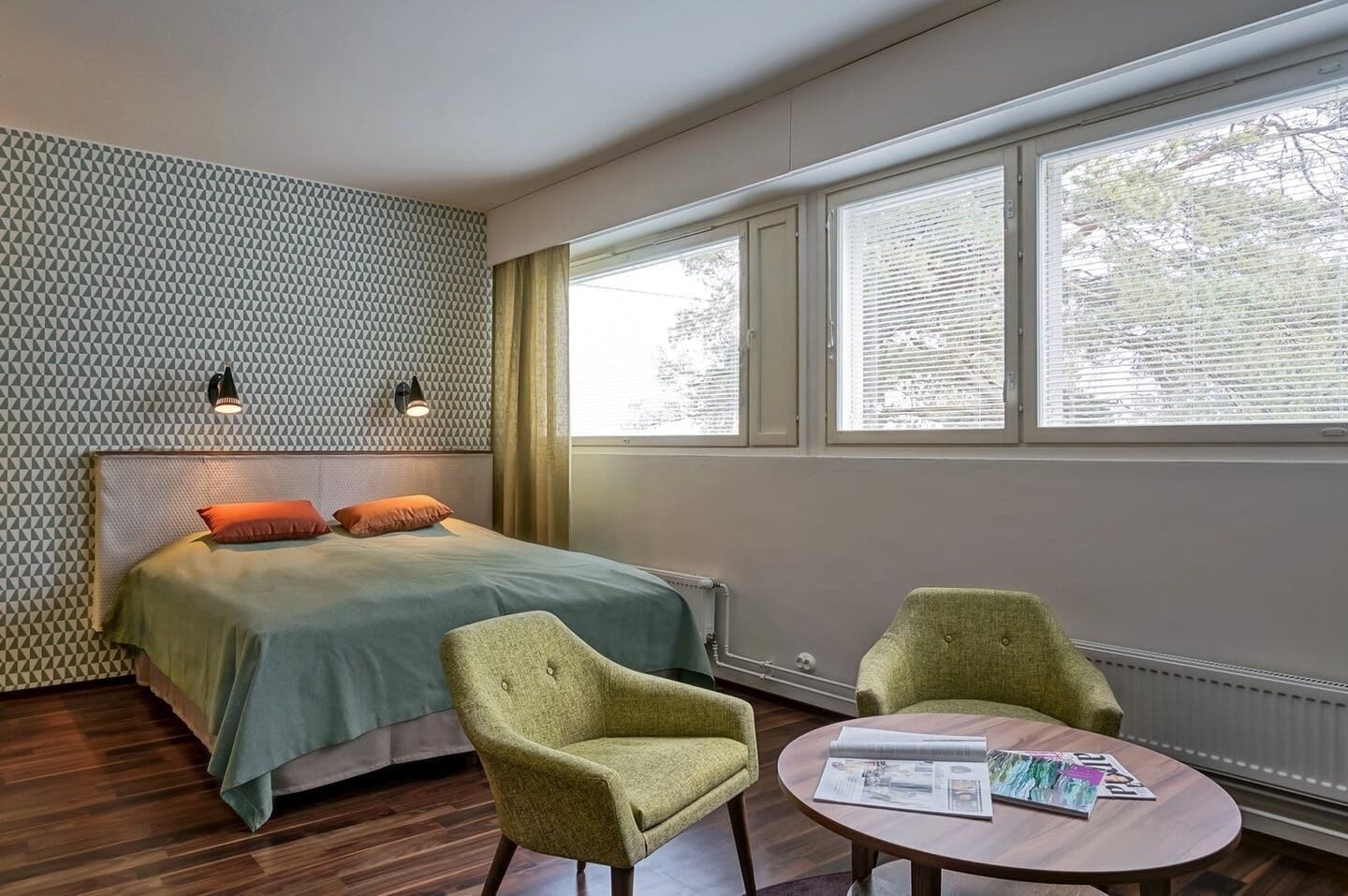 Ein Schlafzimmer mit einem Bett, zwei Stühlen, einem Tisch und einem Fenster mit Jalousien.