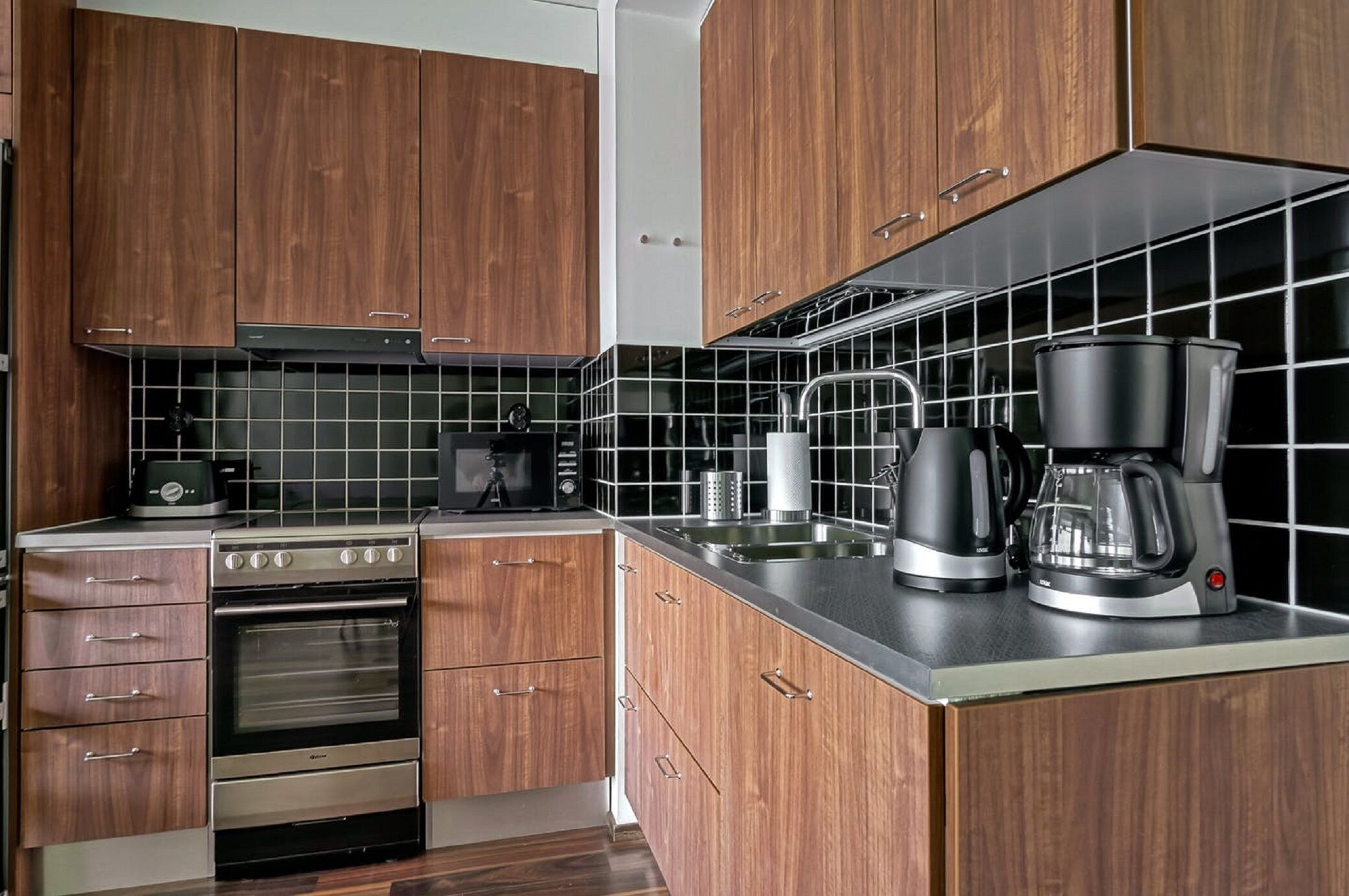 A modern kitchen with wooden cabinets, a stainless steel oven, a coffee maker, and a kettle.