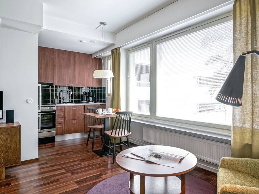 Una cocina moderna con armarios de madera, un comedor con mesa y sillas, y un ventanal con persianas.