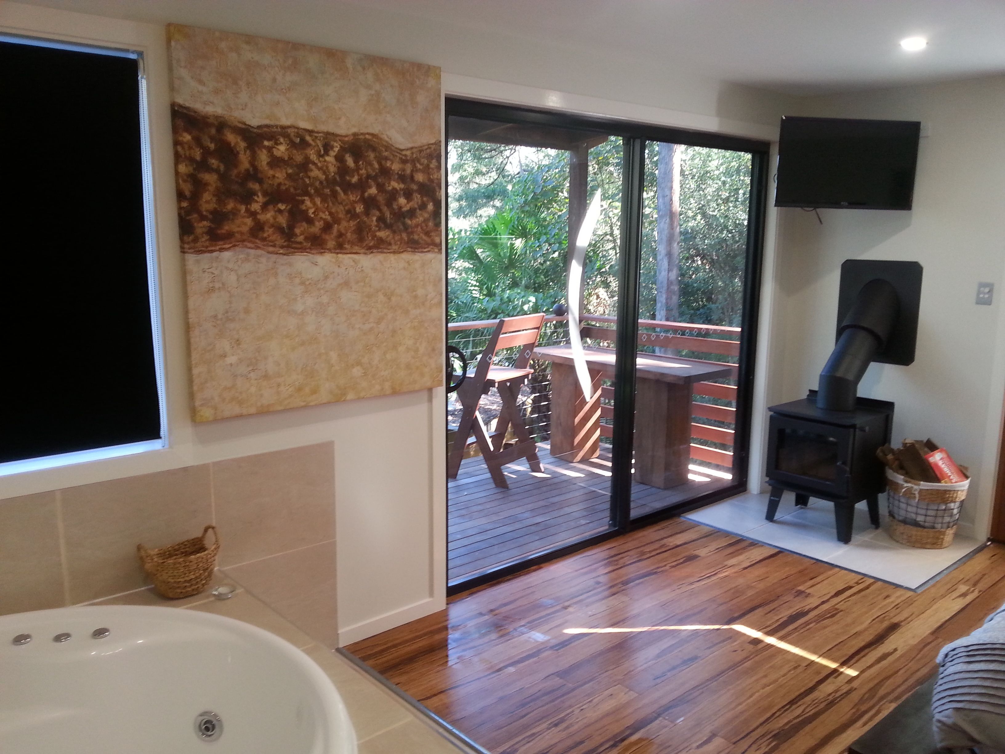 Une salle de bain avec une baignoire, un plancher en bois, une grande fenêtre et une porte-fenêtre coulissante donnant sur une terrasse extérieure.