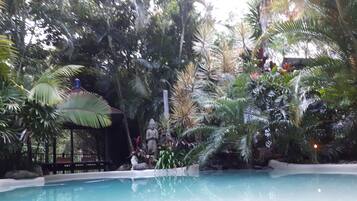 Relax by the serene pool surrounded by lush tropical vegetation and a Buddha statue.