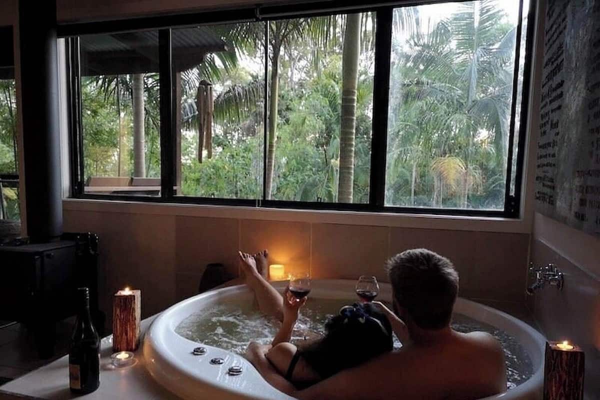 A person relaxing in a hot tub with a view of tropical foliage through large windows.