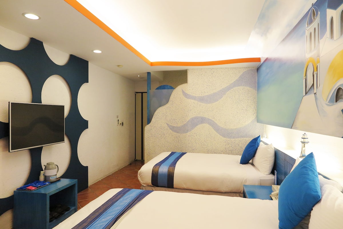 Habitación de hotel con dos camas, televisión, una mesita con hervidor y una pared con diseño de olas.
