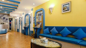 Un área de recepción con un sofá azul, una mesa de centro de vidrio y un suelo de baldosas.
