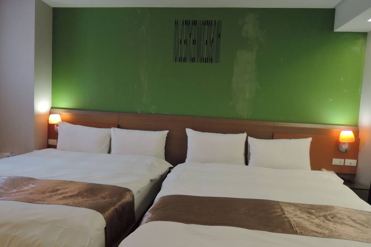 A hotel room with two beds, a green wall, and a headboard.