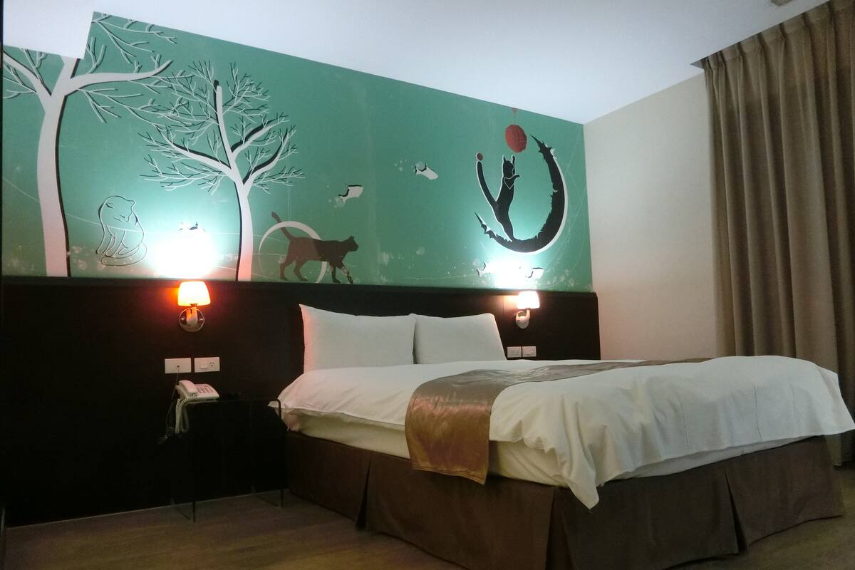 A hotel room with a bed, a nightstand with a phone, and a wall mural.