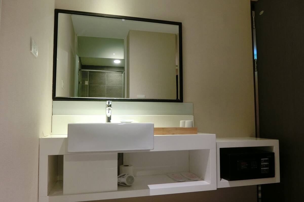 A modern bathroom with a white sink, a mirror, and a built-in microwave.