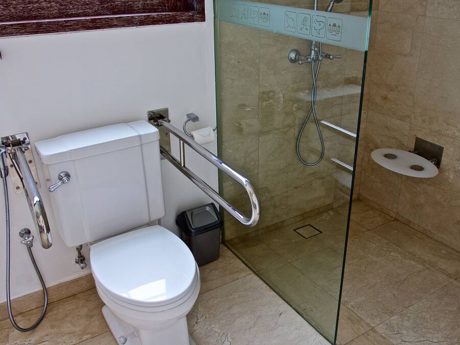 A bathroom with a white toilet, a glass shower enclosure, and a handrail.