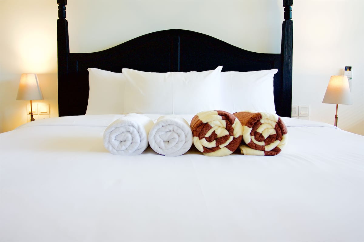 A neatly made bed with white linens and rolled towels in white and brown.