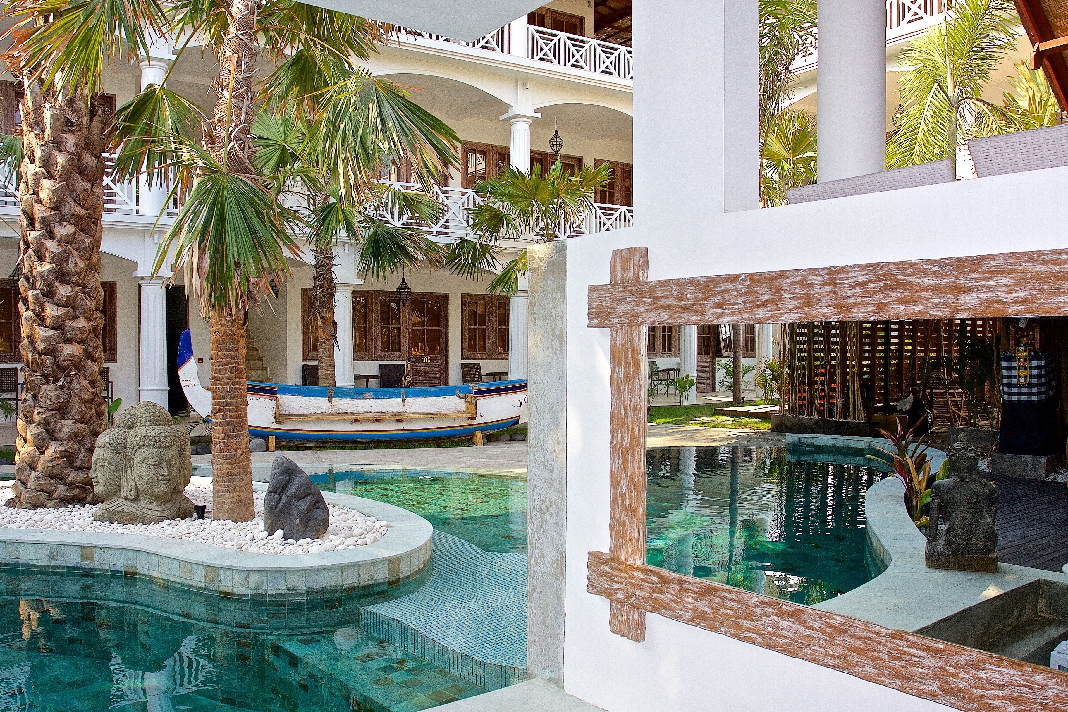 A pool area with a stone Buddha statue, palm trees, and a wooden deck.