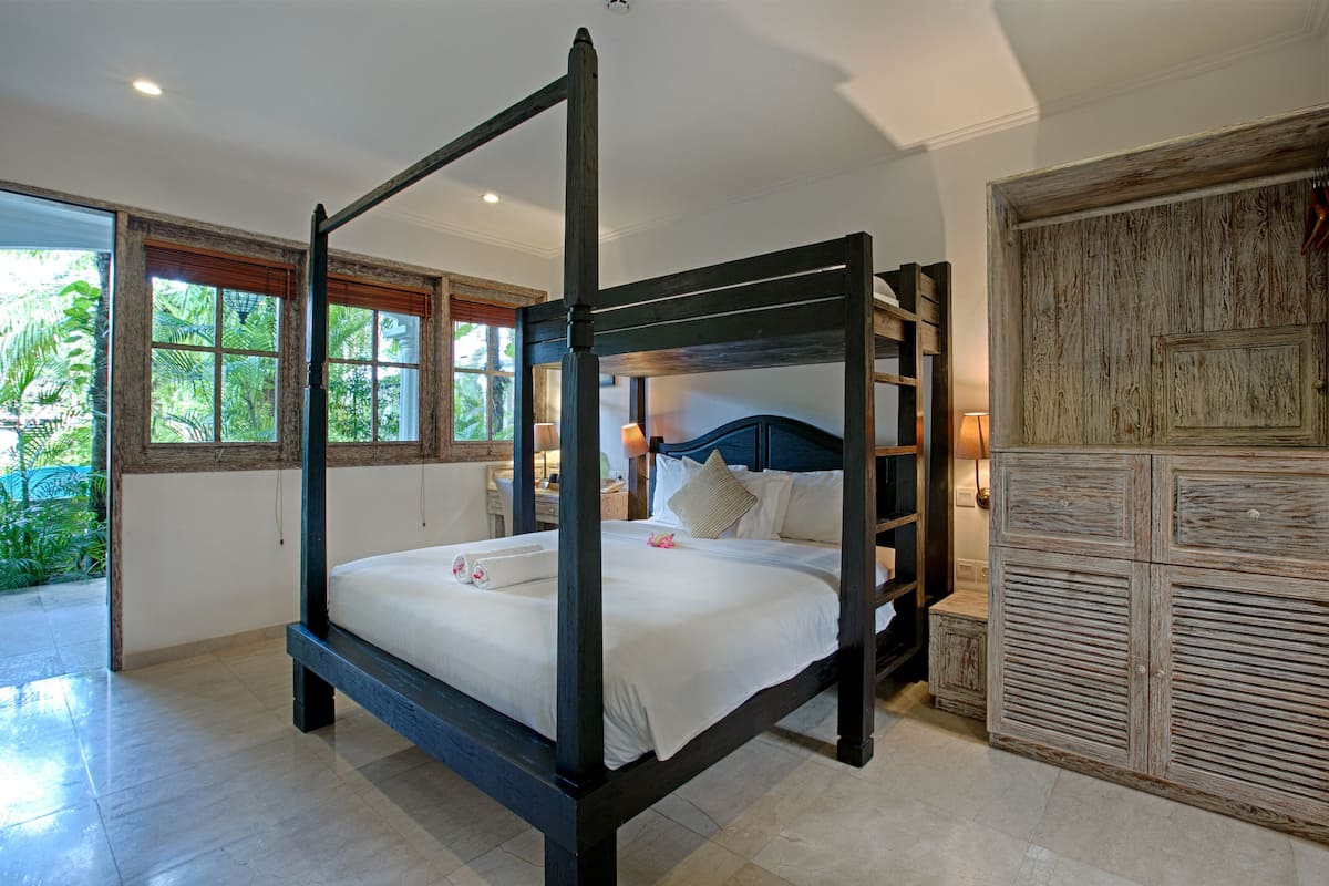 A four-poster bed with a wooden frame, white bedding, and a bedside table with a lamp.