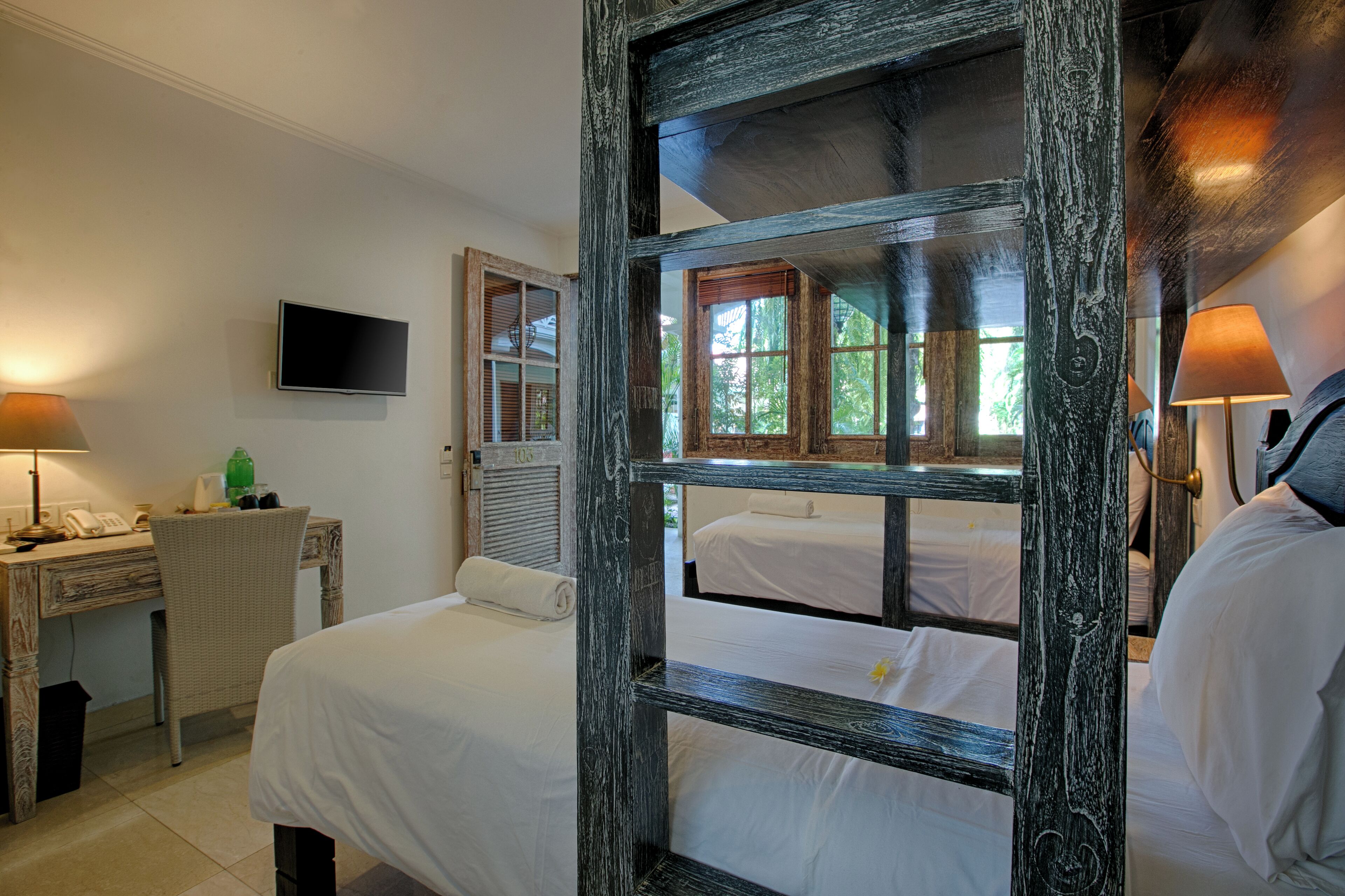 Habitación de hotel con una cama grande, un escritorio con teléfono, televisión montada en la pared y ventana con vistas a la vegetación.