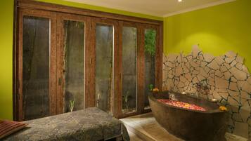 Unwind in a serene spa room with a bathtub, surrounded by candles and a view of lush greenery.