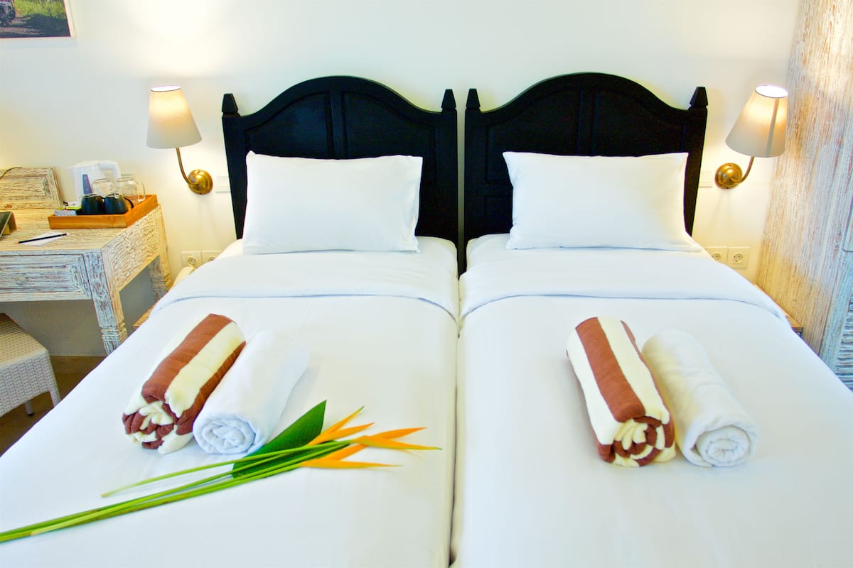 A double bed with white linens and two rolled towels on each side.