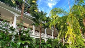 A hotel with a covered outdoor area featuring palm trees and a white balcony railing. - OK Divers Resort & Spa (Padangbai)