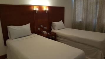 Habitación de hotel con dos camas individuales, cabecero de madera, mesita de noche con teléfono e iluminación de techo.