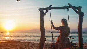 Escena de playa con un columpio y una puesta de sol al fondo.