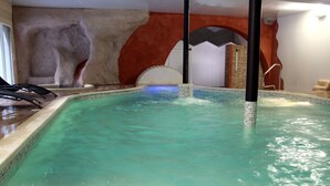 Una piscina interior con agua cristalina, borde de azulejos y un muro de piedra de fondo.