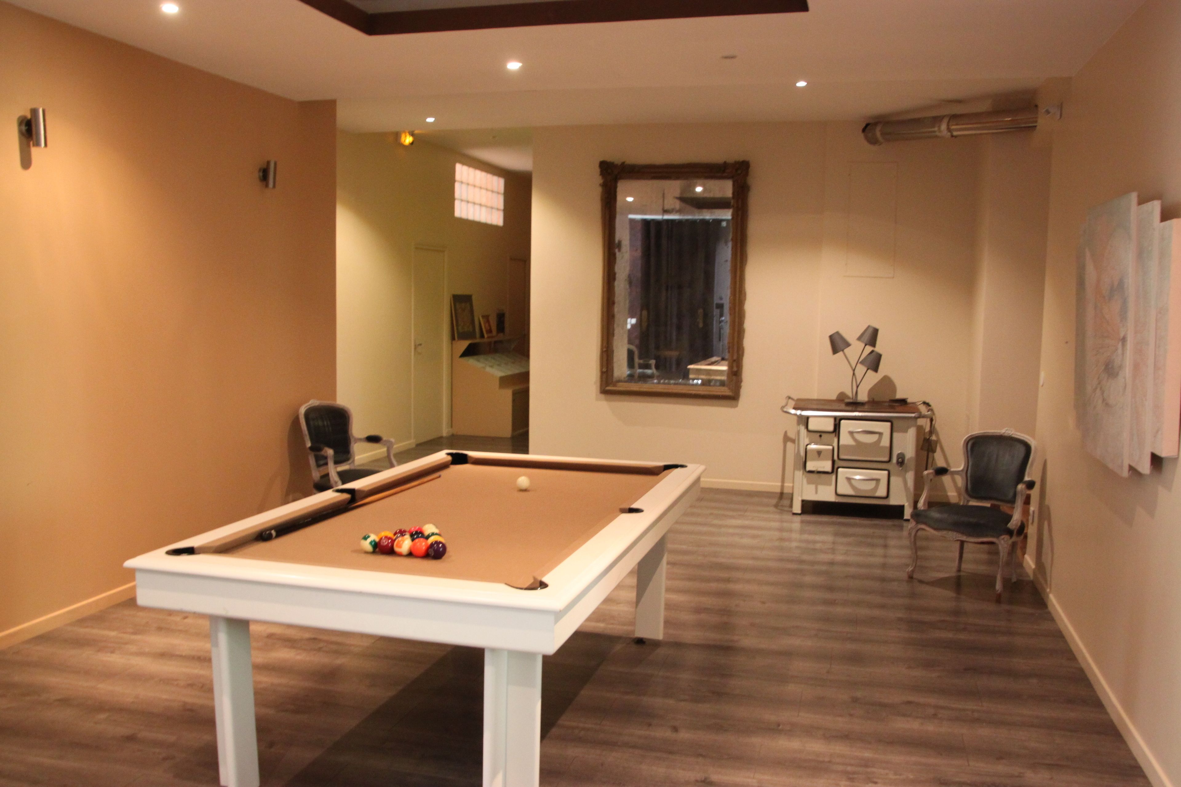 A pool table in a room with wooden flooring, a mirror on the wall, and a small desk with drawers.