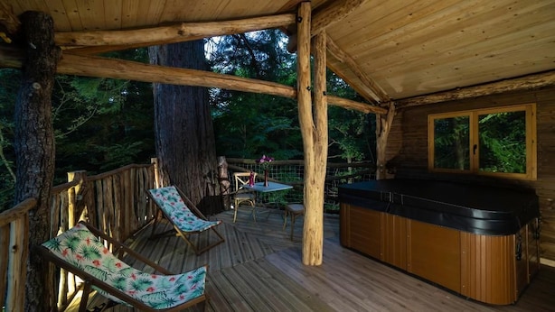 Una terraza de madera con un jacuzzi, sillas de descanso y una mesa.