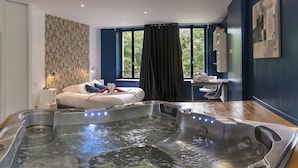 Un spa moderno con jacuzzi, un sofá con cojines y vistas a la vegetación a través de amplias ventanas.
