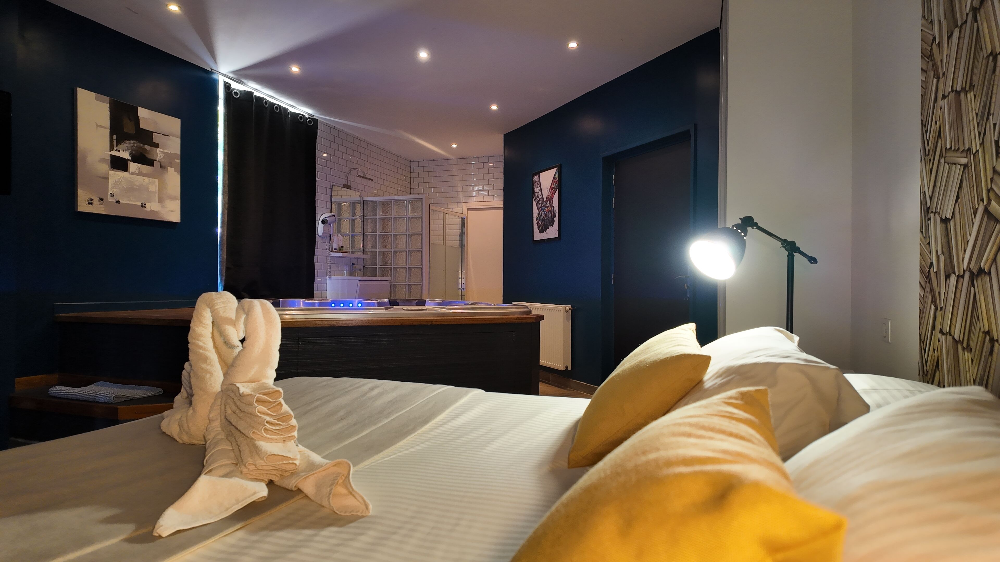 A hotel room with a bed, a desk, a lamp, and a bathroom visible through an open door.