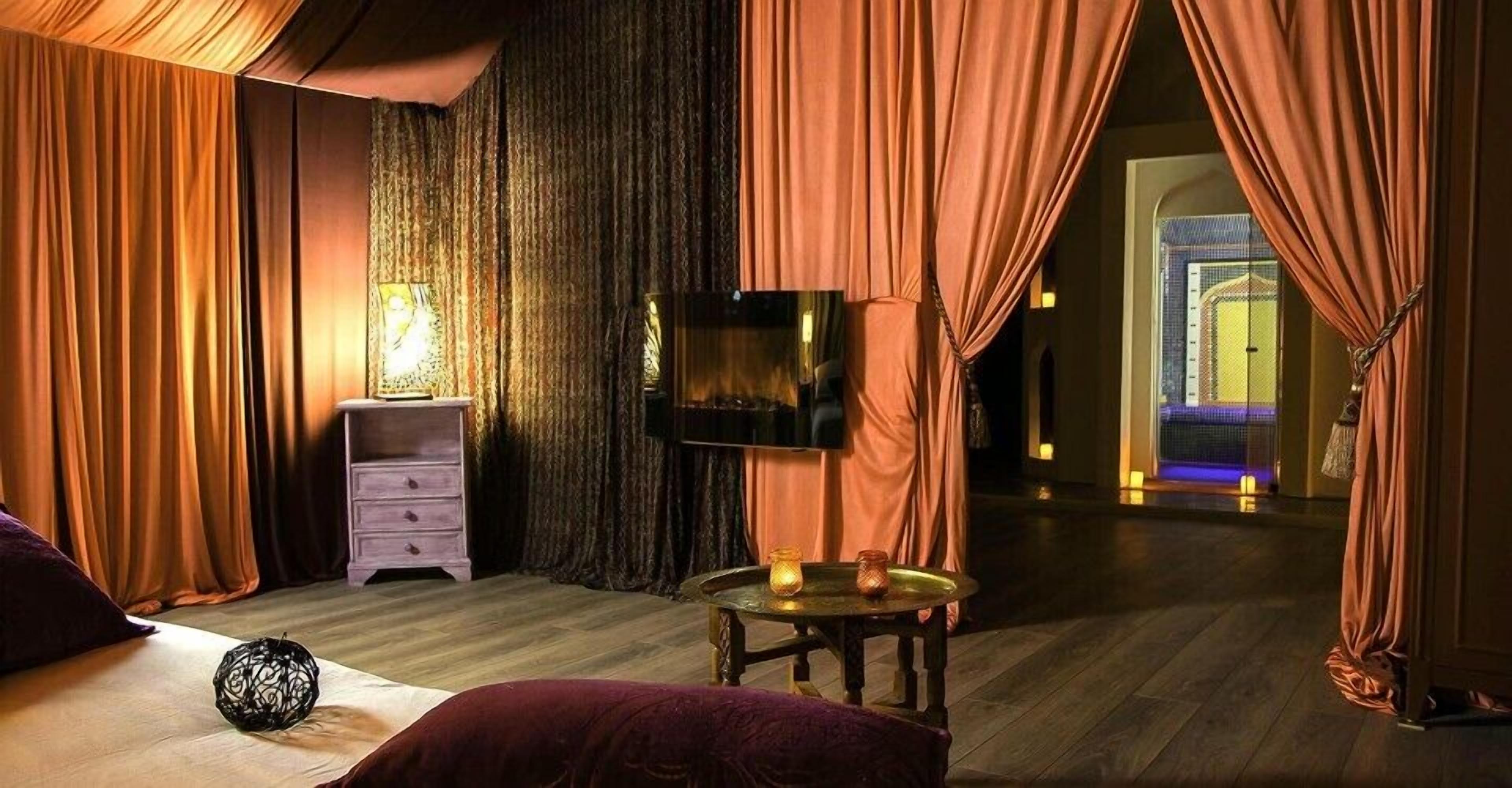 Una habitación tenuemente iluminada con una cama, una mesita con velas, un televisor y un aparador.