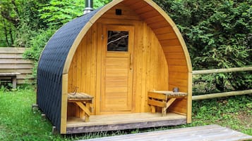 Une cabane en bois avec un toit à deux versants, une cheminée et un petit porche doté de deux bancs.
