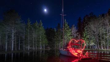 A boat docked at night with a clear view of the moon and a forested shoreline.