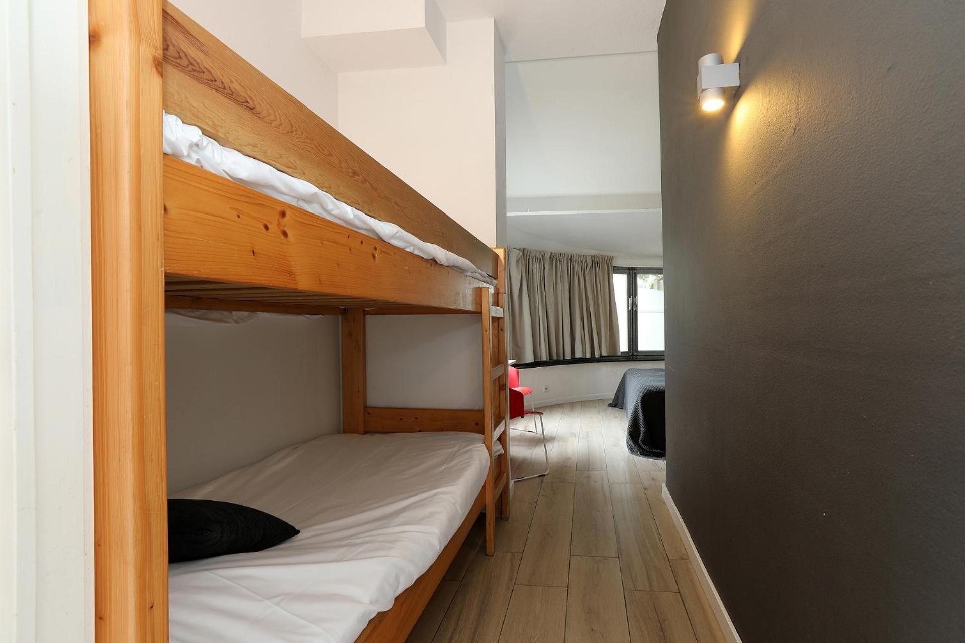 A bunk bed room with a window, a red chair, and a wall-mounted light fixture.
