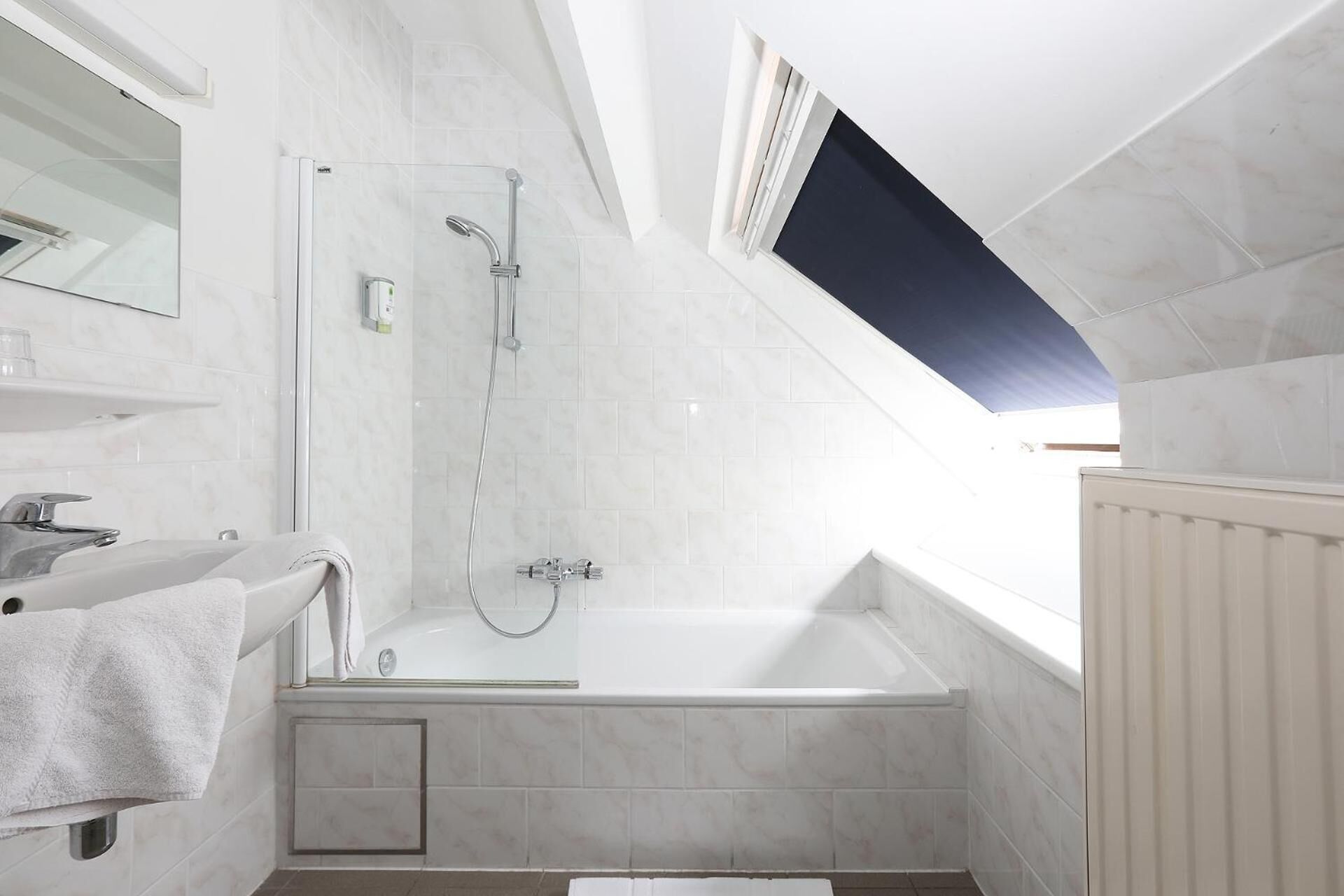 Ein modernes Badezimmer mit Oberlicht, einer Badewanne, einer Dusche und einem Waschtisch mit Spiegel.