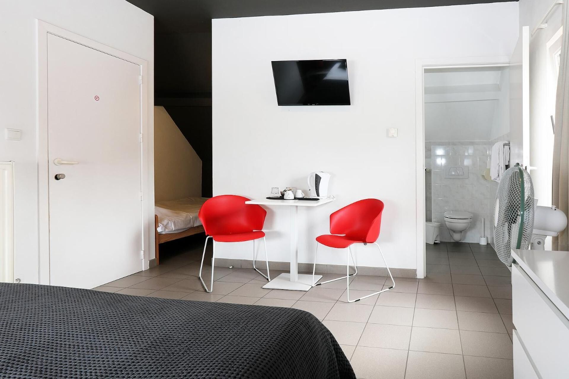 A compact room with a bed, a small table with chairs, a TV, and a bathroom visible through an open door.