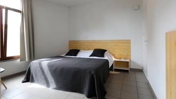 A hotel room with a bed, a nightstand, a lamp, a window with curtains, and a door.