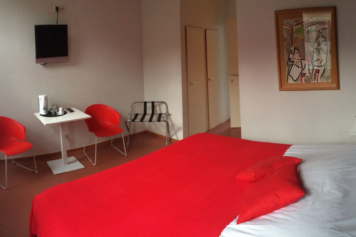 A hotel room with a large bed, a desk with a chair, a TV, and a painting on the wall.