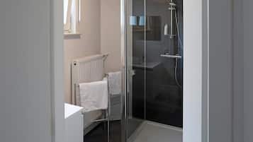 Un baño moderno con cabina de ducha de vidrio, un radiador blanco y un perchero para toallas.