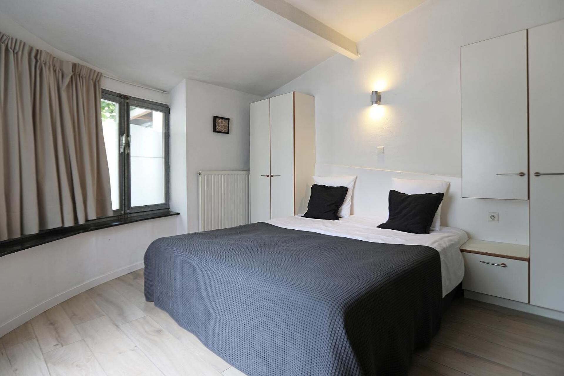 Une chambre à coucher comprenant un lit, une table de chevet, une armoire et une fenêtre avec des rideaux.