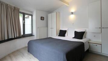 Une chambre à coucher comprenant un lit, une table de chevet, une armoire et une fenêtre avec des rideaux.