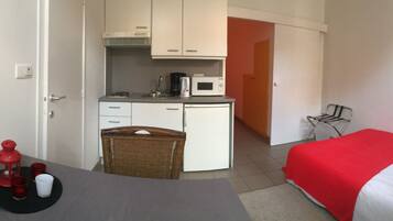 A compact hotel room with a kitchenette, a dining area, and a bed with red bedding.