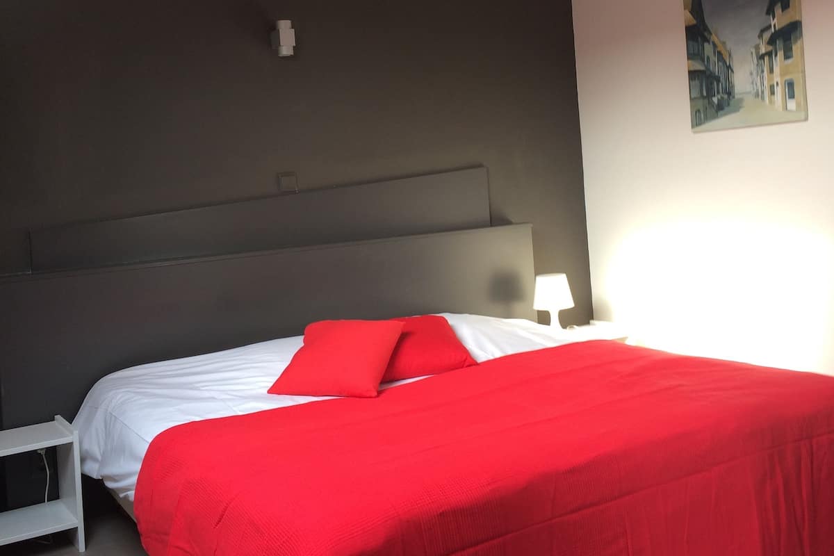 A bedroom with a bed, a nightstand, a painting, and a ceiling light.