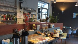 Un buffet de petit-déjeuner proposant une variété d’aliments, un coin café et un bar avec des étagères remplies de bouteilles et de verres.