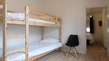 Une chambre avec un lit superposé, une chaise noire et une porte donnant sur une autre pièce.