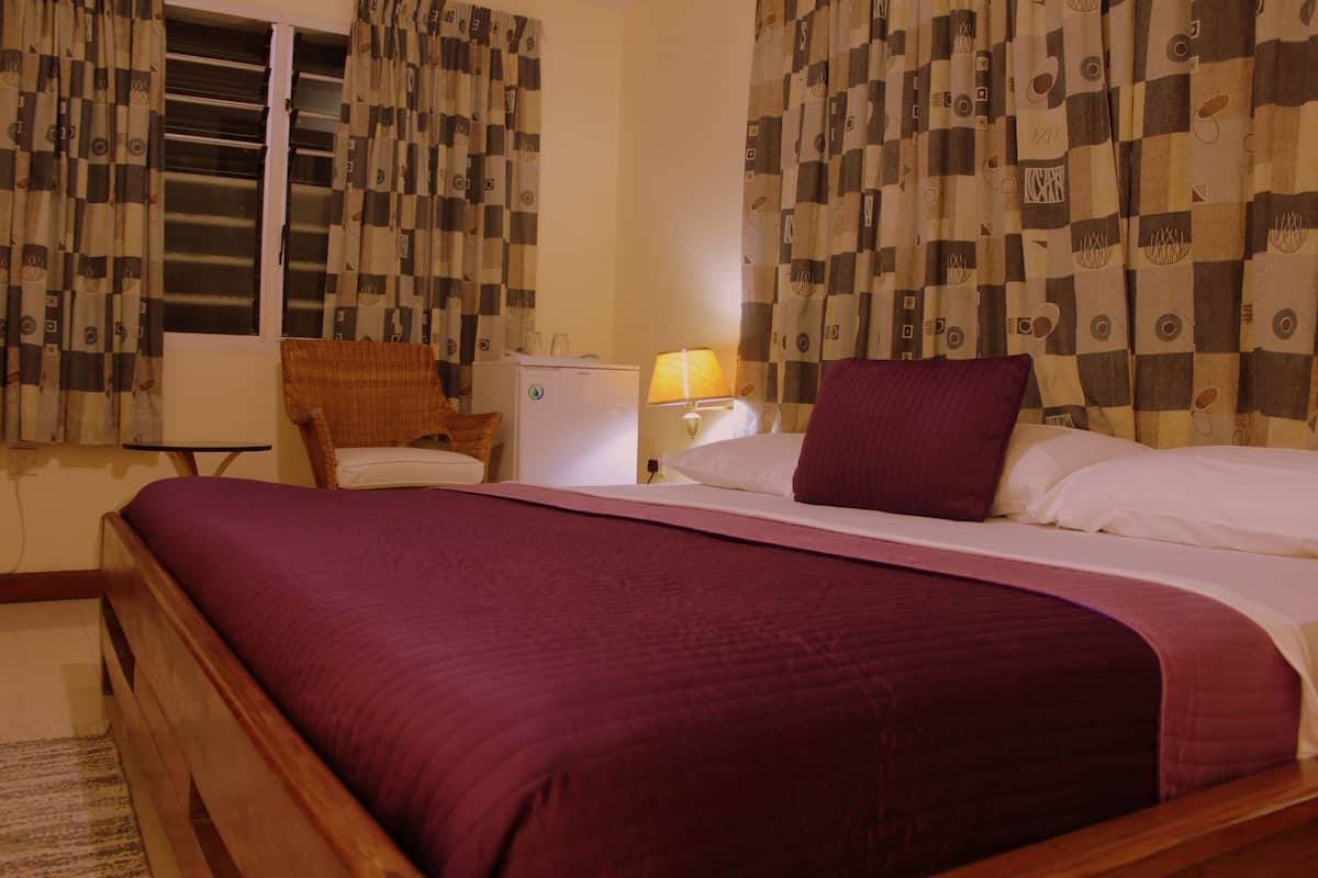 A hotel room with a bed, a chair, a small table, a lamp, and curtains.