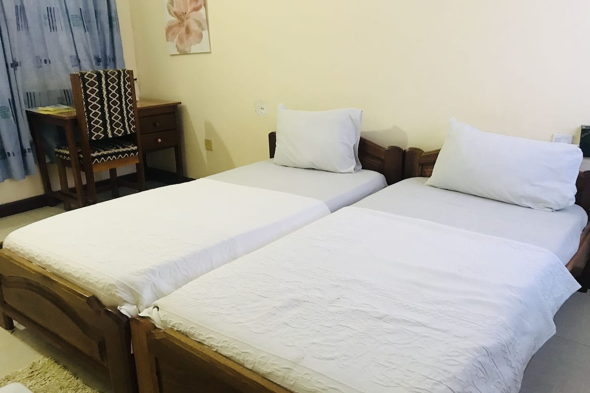 A double bed with white linens, a wooden headboard, and a bedside table with a lamp.