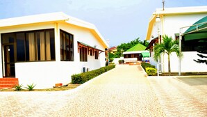 A pathway leading to a building with a reception area, surrounded by greenery and palm trees. - Hotel Loreto (Cape Coast)