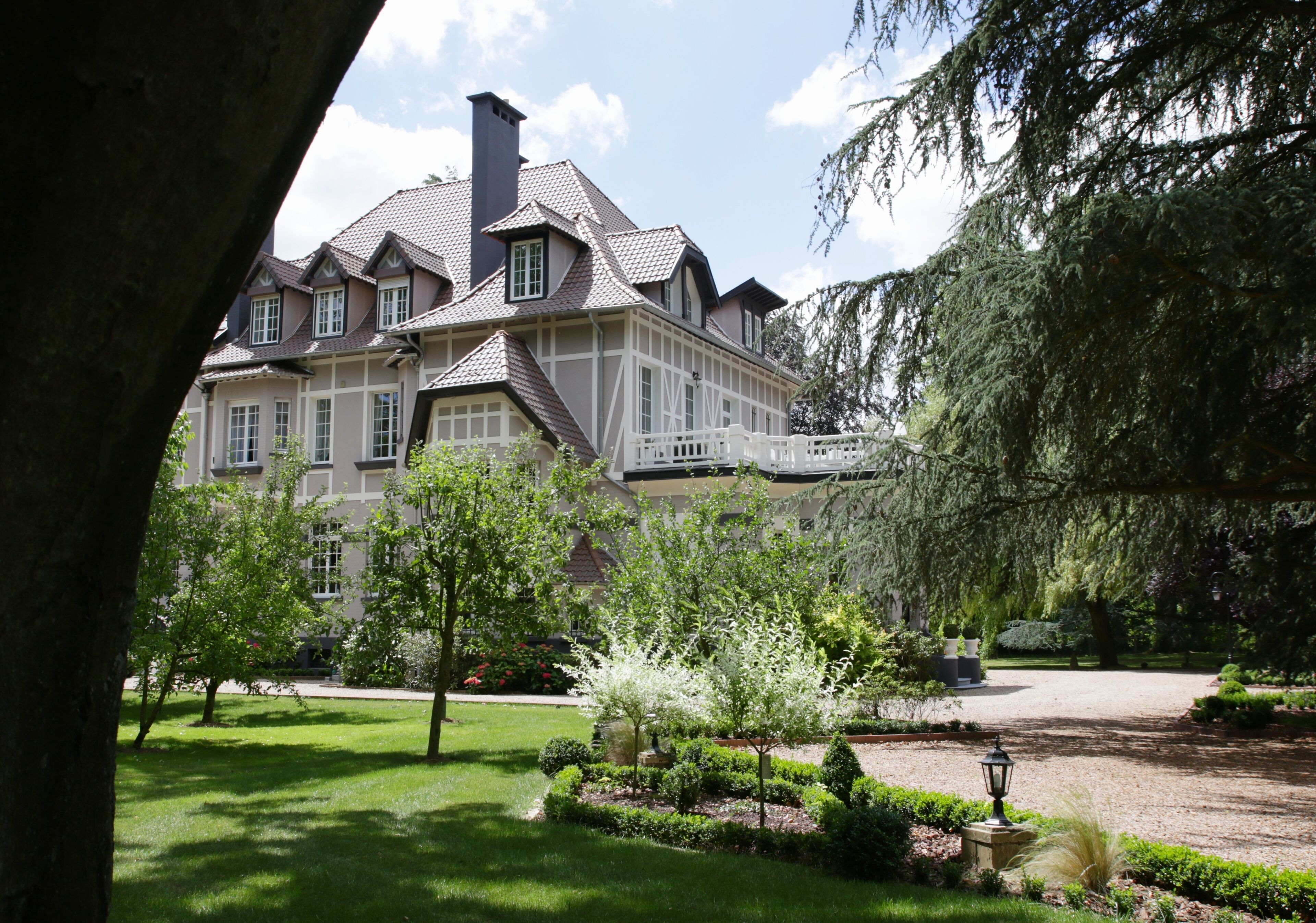 A large, two-story house with a symmetrical facade, a central chimney, and a well-maintained garden with various shrubs and a lawn.
