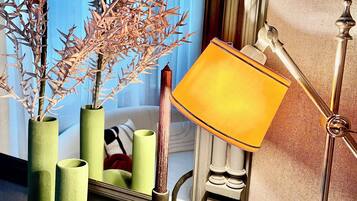 Een kamer met een spiegel die een bed, een lamp en groene vazen met takken weerkaatst.