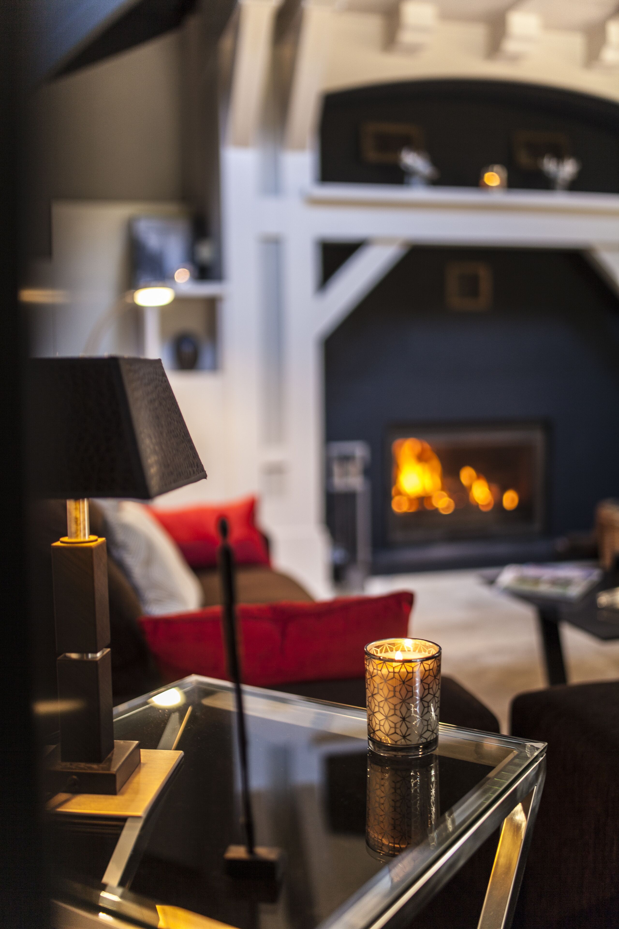 A modern living room with a glass coffee table, a lamp, and a lit candle.