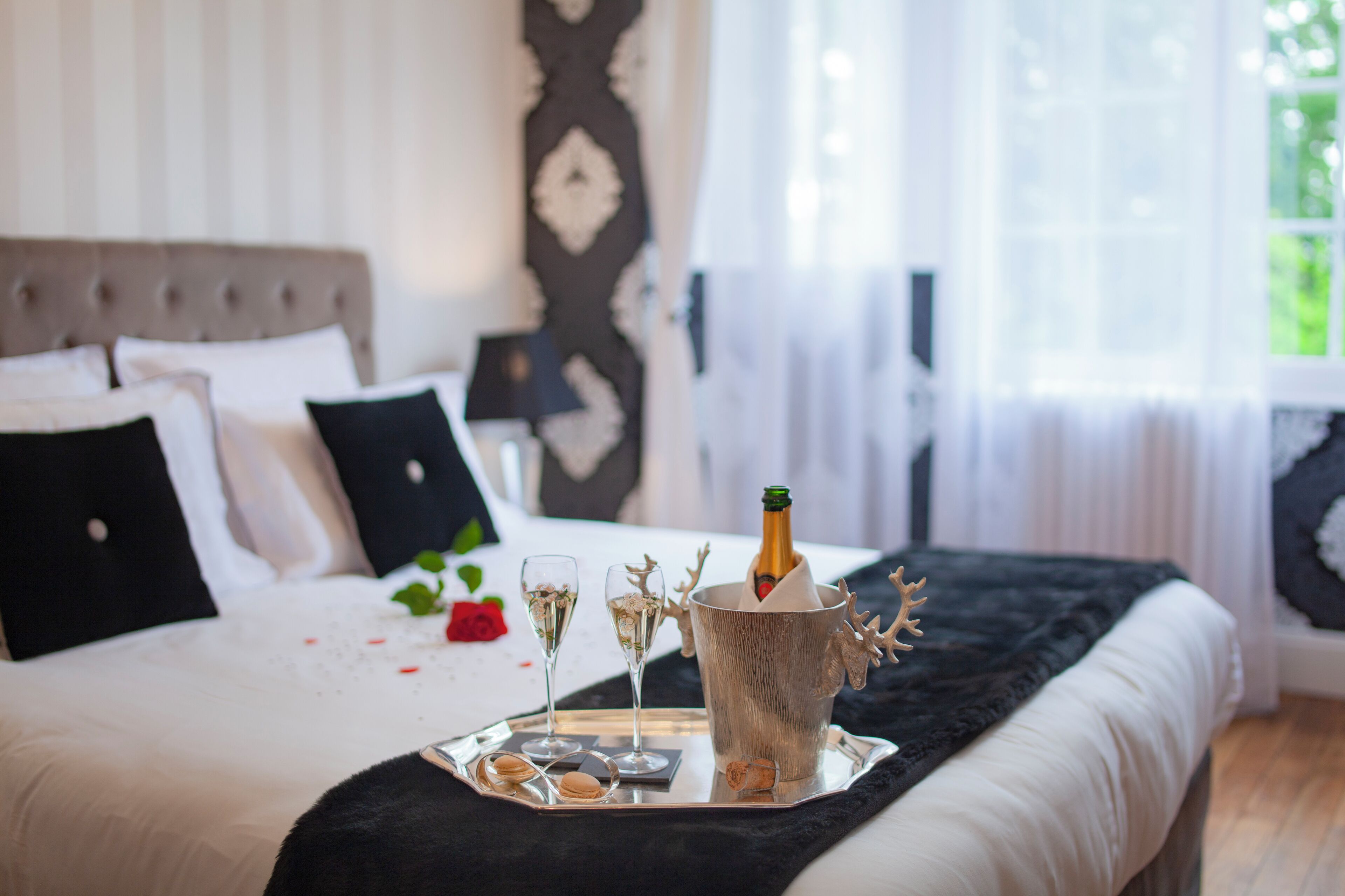 A bed with a champagne bottle, glasses, and snacks on a tray.